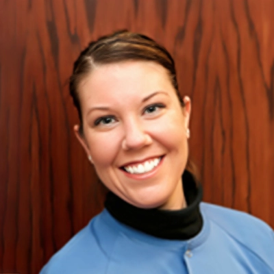 Registered Dental Hygienist Kelly Smiling In Scrubs In Front Of Wood Wall