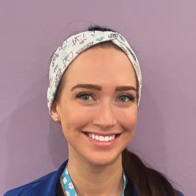 Brooke smiling at the camera while wearing blue scrubs and a patterned headband